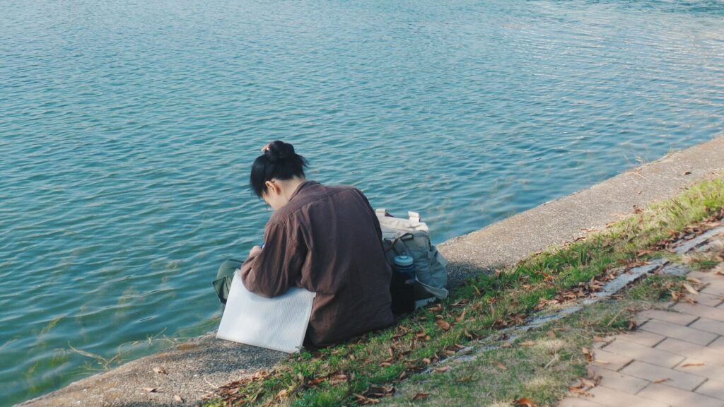 woman in brown shirt sitting on white concrete bench near body of water during daytime