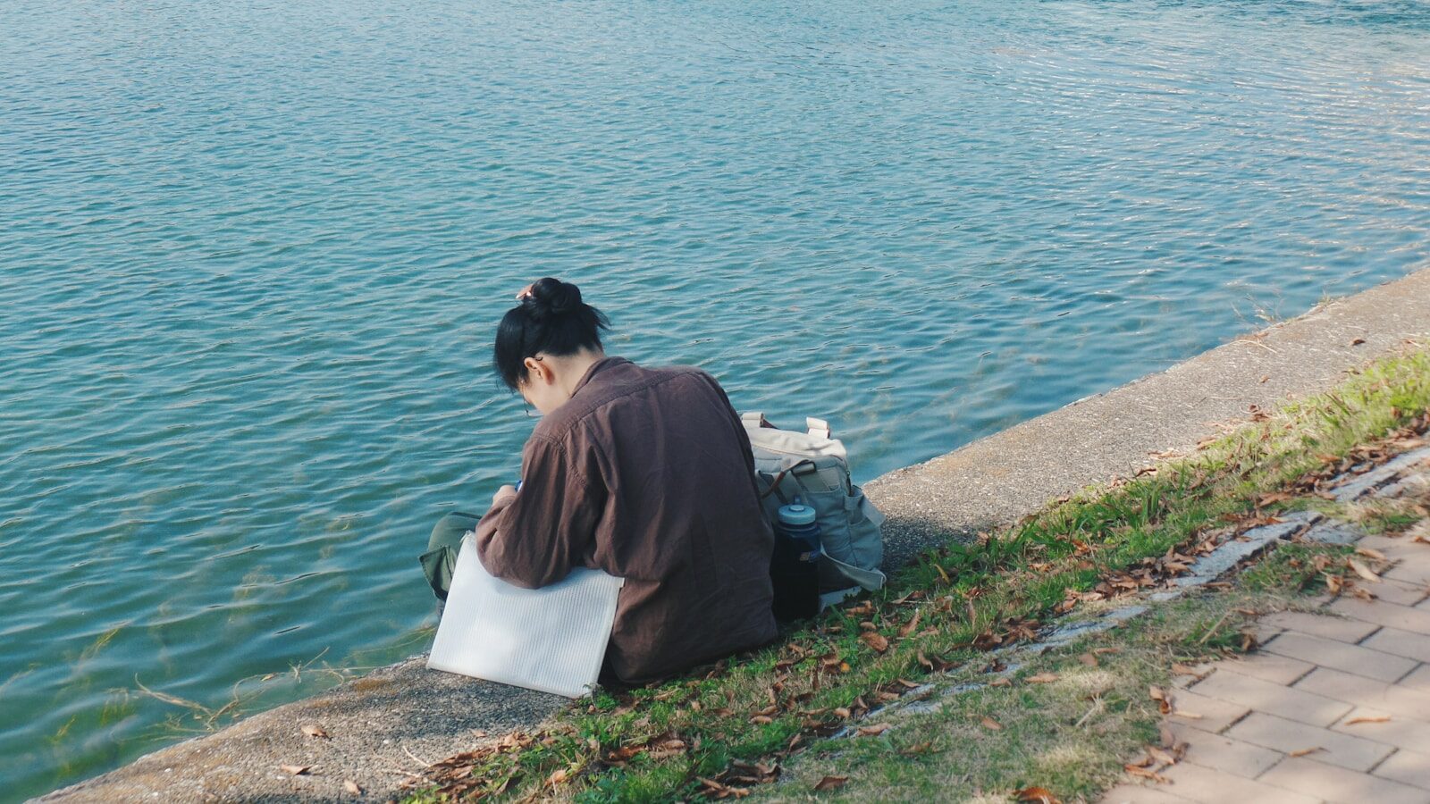 woman in brown shirt sitting on white concrete bench near body of water during daytime