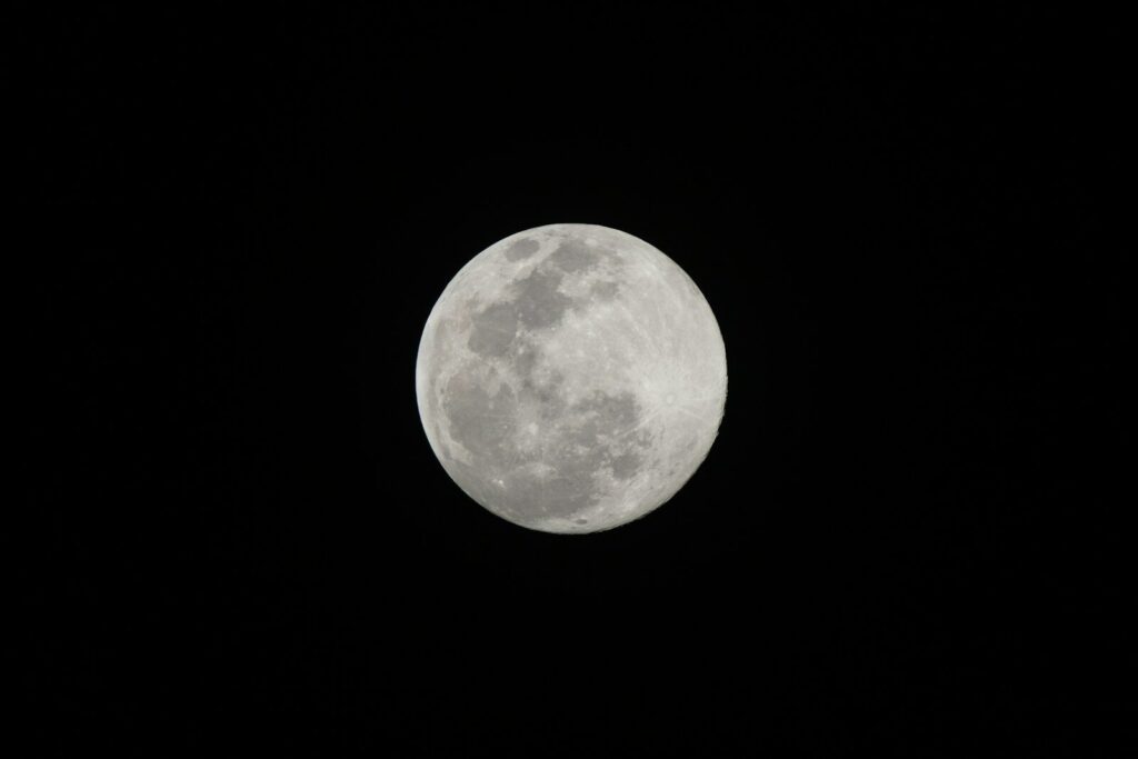 A full moon is seen in the dark sky